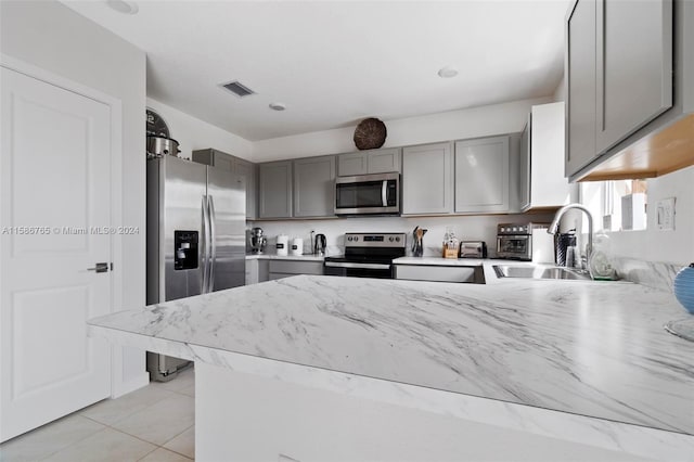 kitchen featuring gray cabinetry, sink, light tile patterned flooring, kitchen peninsula, and appliances with stainless steel finishes