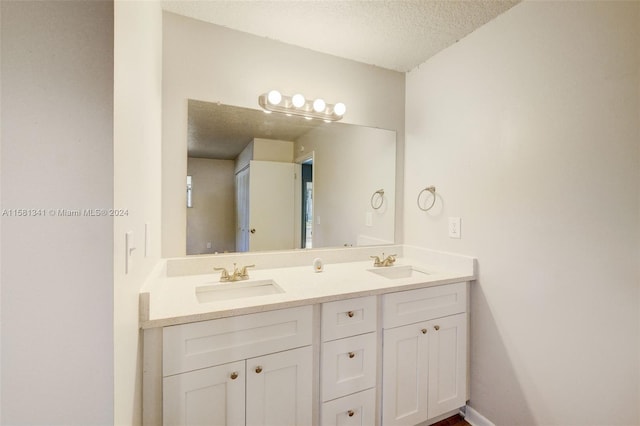 bathroom featuring a textured ceiling, vanity with extensive cabinet space, and dual sinks