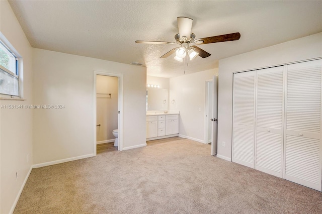 unfurnished bedroom featuring ceiling fan, ensuite bathroom, a closet, and light carpet