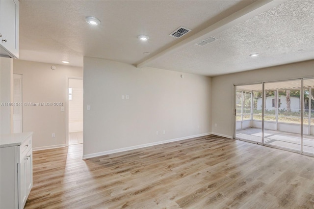 empty room with beamed ceiling, a textured ceiling, and light wood-type flooring