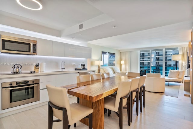 dining area featuring sink, light hardwood / wood-style flooring, and a tray ceiling