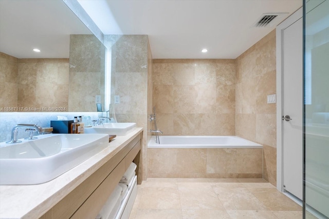 bathroom with dual bowl vanity, tile flooring, tiled bath, and tile walls