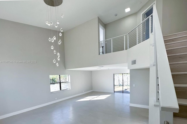 unfurnished living room featuring a towering ceiling, plenty of natural light, and a notable chandelier