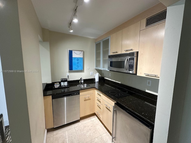 kitchen featuring kitchen peninsula, stainless steel appliances, dark stone counters, light tile patterned floors, and light brown cabinetry