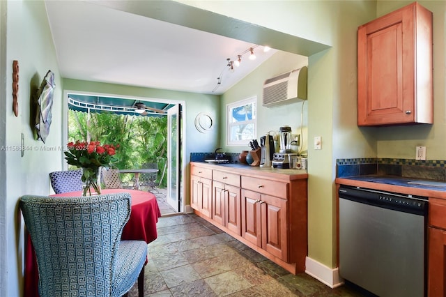 kitchen featuring baseboards, a wall mounted air conditioner, stone finish flooring, dishwasher, and dark countertops