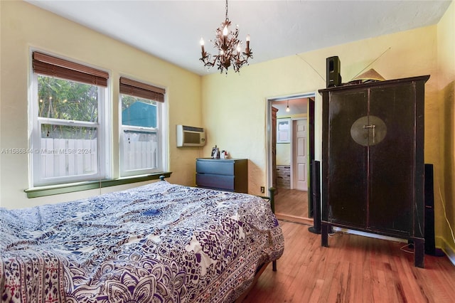 bedroom featuring a wall unit AC, a notable chandelier, and wood finished floors