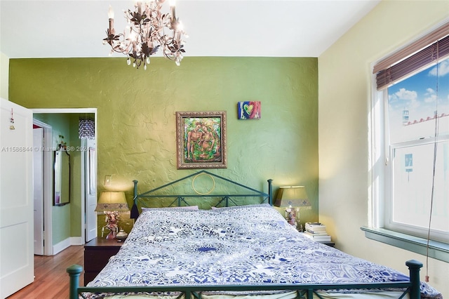 bedroom with a notable chandelier, baseboards, a textured wall, and wood finished floors