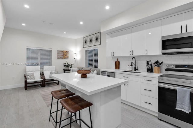 kitchen with a breakfast bar, sink, white cabinetry, appliances with stainless steel finishes, and a kitchen island