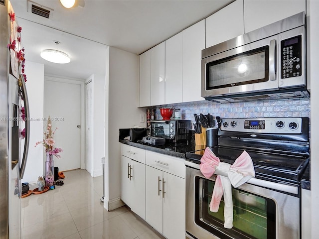 kitchen with dark stone counters, stainless steel appliances, backsplash, light tile floors, and white cabinets