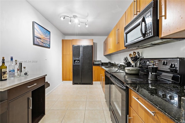 kitchen with dark stone counters, rail lighting, black appliances, sink, and light tile floors