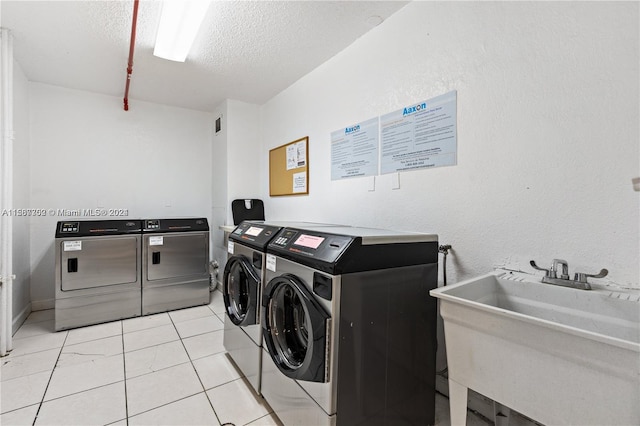 washroom featuring sink, washing machine and dryer, light tile flooring, and a textured ceiling