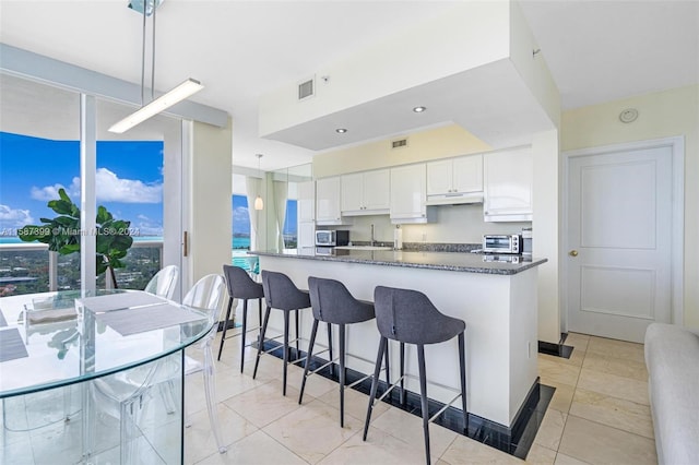 kitchen with a kitchen breakfast bar, light tile flooring, pendant lighting, dark stone countertops, and white cabinetry