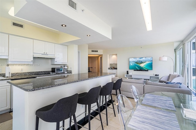 kitchen featuring a kitchen island, a kitchen breakfast bar, dark stone countertops, white cabinets, and light tile floors