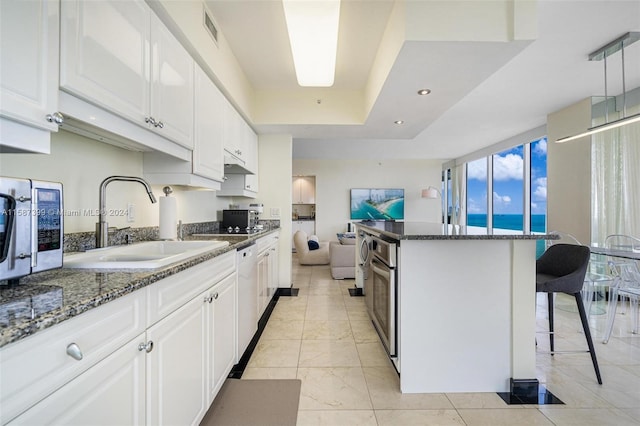 kitchen with dark stone counters, a raised ceiling, light tile floors, sink, and white cabinets