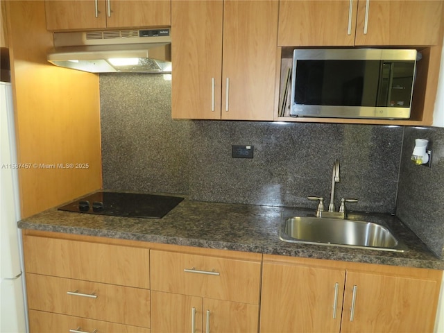 kitchen with black electric stovetop, stainless steel microwave, decorative backsplash, a sink, and under cabinet range hood