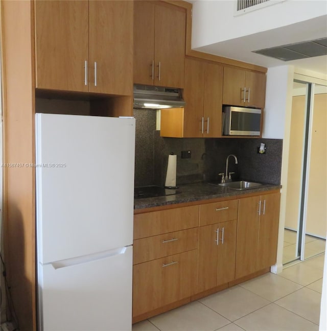 kitchen featuring light tile patterned floors, under cabinet range hood, a sink, freestanding refrigerator, and tasteful backsplash