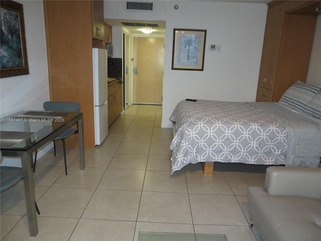 bedroom with light tile patterned floors, visible vents, and freestanding refrigerator