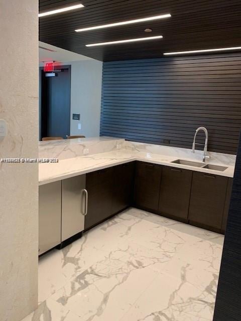 kitchen with a sink, light marble finish floors, and dark brown cabinets