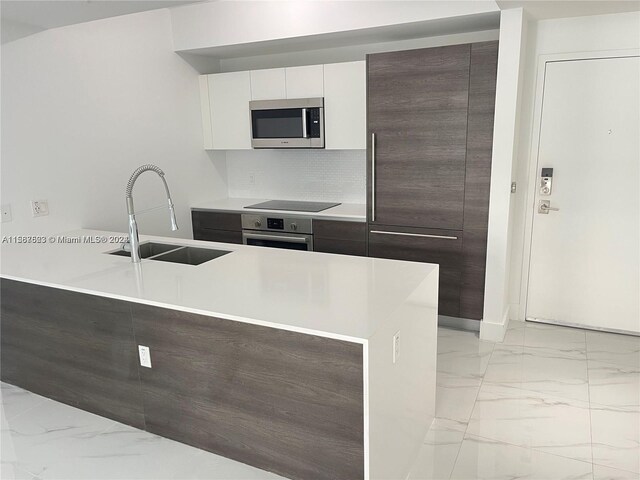 kitchen featuring stainless steel appliances, light marble finish flooring, a sink, light countertops, and tasteful backsplash