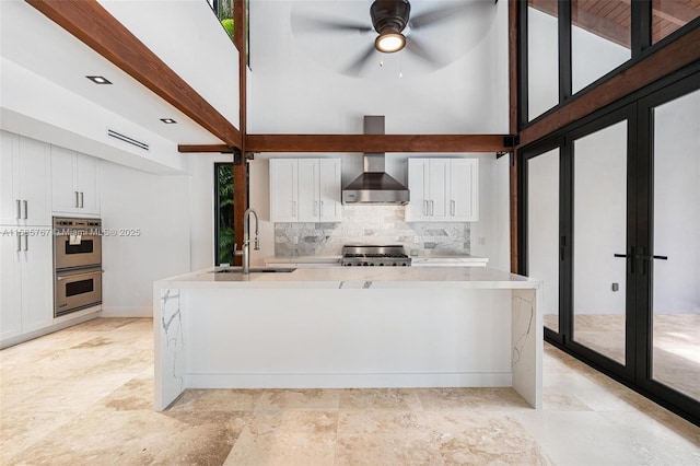 kitchen with stove, sink, wall chimney range hood, and white cabinets