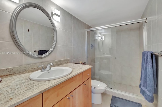 bathroom featuring tile flooring, toilet, tile walls, a shower with door, and oversized vanity