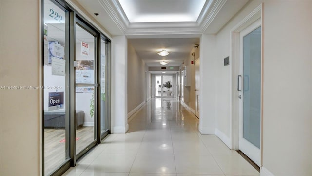 hallway featuring a tray ceiling, ornamental molding, and light tile floors