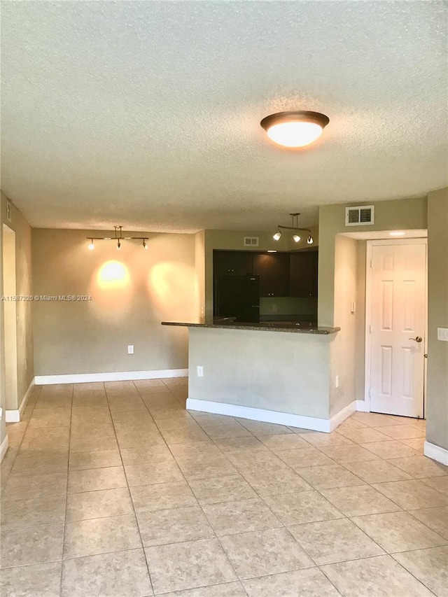 empty room with a textured ceiling, track lighting, and light tile floors