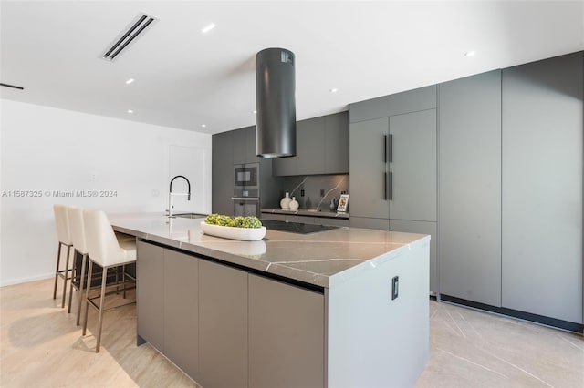 kitchen with sink, gray cabinets, dark stone counters, and a large island with sink