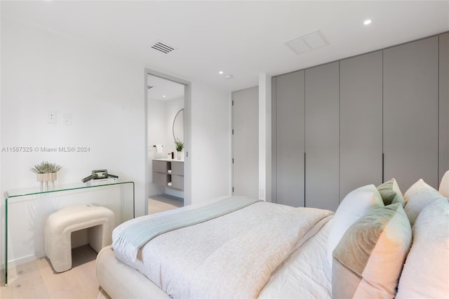 bedroom with ensuite bathroom, light hardwood / wood-style floors, and a closet