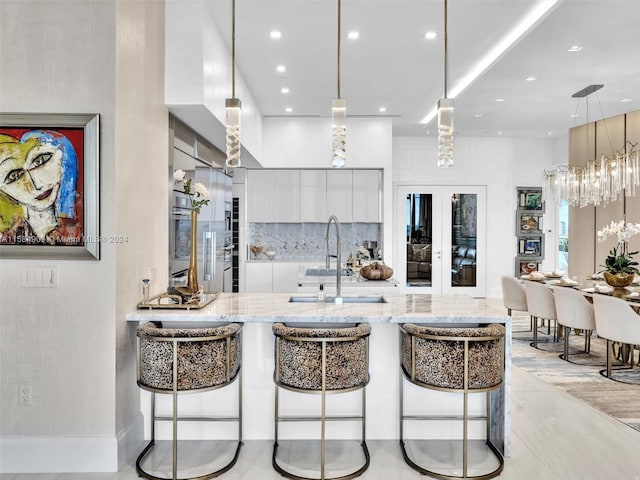 kitchen featuring light stone countertops, french doors, hanging light fixtures, sink, and white cabinets