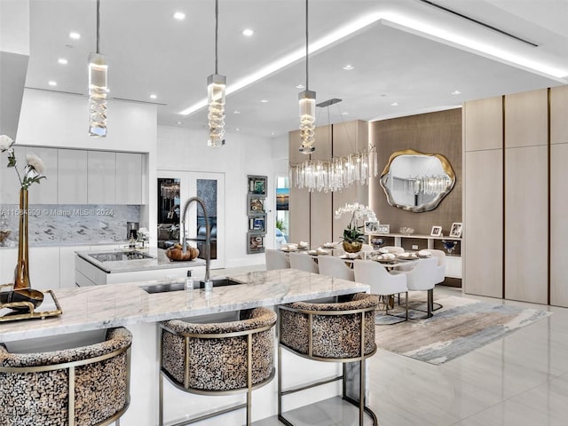 kitchen featuring decorative light fixtures, light stone counters, a kitchen breakfast bar, sink, and light tile floors