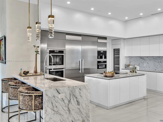 kitchen featuring a kitchen island, backsplash, hanging light fixtures, white cabinetry, and light tile floors