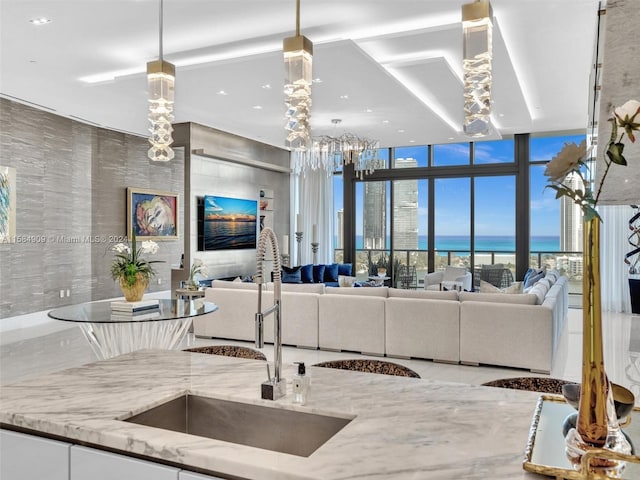 kitchen featuring a water view, light stone counters, hanging light fixtures, floor to ceiling windows, and white cabinets