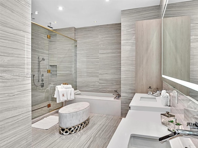 bathroom with plus walk in shower, tile walls, oversized vanity, and double sink