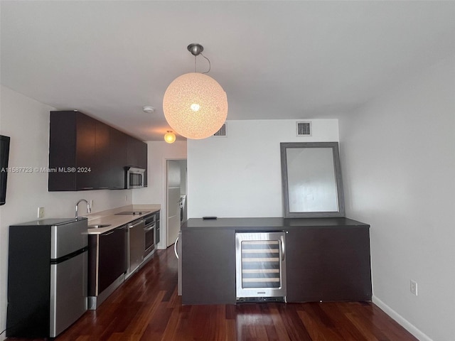 kitchen featuring dark hardwood / wood-style flooring, appliances with stainless steel finishes, beverage cooler, sink, and dark brown cabinetry