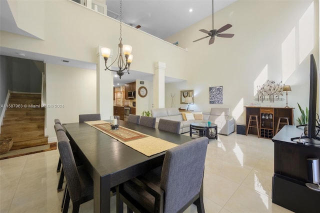 dining space with a towering ceiling, ceiling fan with notable chandelier, decorative columns, and light tile floors