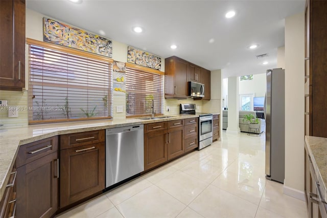 kitchen featuring light tile flooring, stainless steel appliances, tasteful backsplash, light stone countertops, and sink