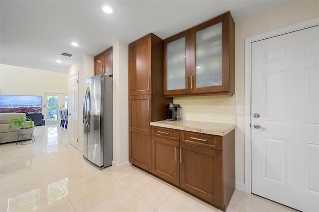 kitchen featuring light stone countertops, stainless steel fridge, tasteful backsplash, and light tile flooring