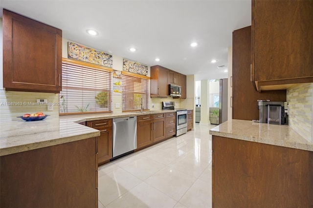 kitchen with kitchen peninsula, backsplash, light stone countertops, appliances with stainless steel finishes, and light tile floors