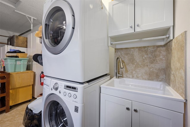 laundry room with light tile floors, sink, stacked washer and dryer, and a textured ceiling