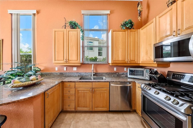 kitchen with light tile patterned floors, appliances with stainless steel finishes, sink, and dark stone counters