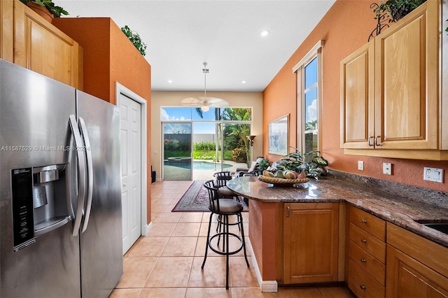 kitchen featuring dark stone counters, stainless steel fridge, a kitchen bar, decorative light fixtures, and light tile patterned floors