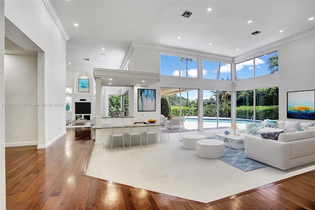 living room with a towering ceiling, ornamental molding, and hardwood / wood-style flooring