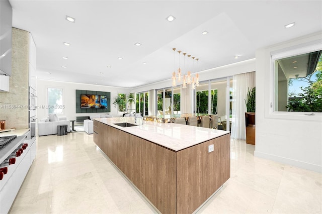 kitchen featuring light stone countertops, sink, white cabinetry, hanging light fixtures, and a large island