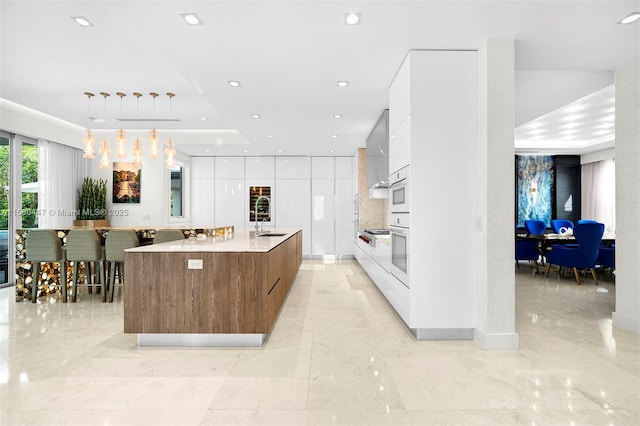 kitchen with a large island, a raised ceiling, oven, decorative light fixtures, and white cabinets