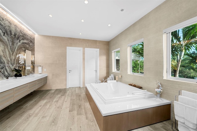 bathroom with hardwood / wood-style floors, vanity, a bath, and tile walls