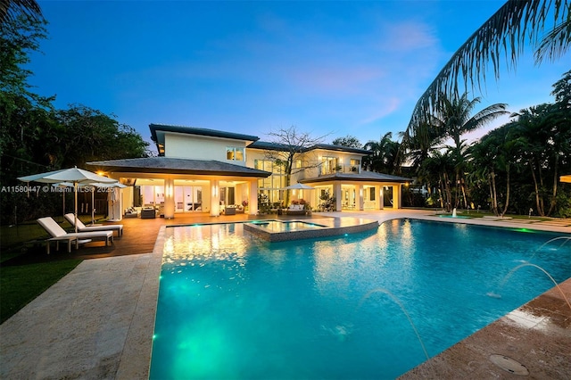 pool at dusk with an in ground hot tub, a patio, and pool water feature