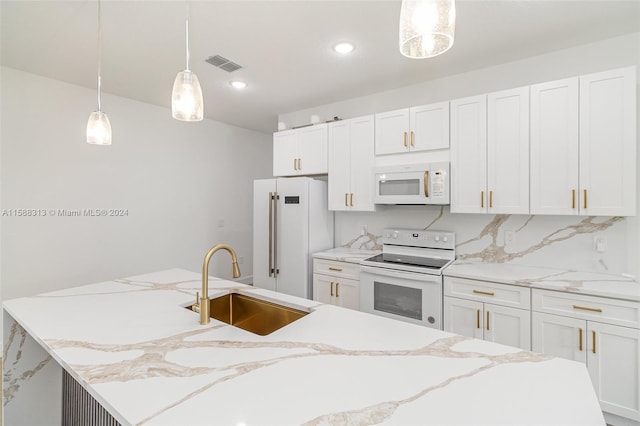 kitchen featuring white appliances, a center island with sink, sink, hanging light fixtures, and white cabinets