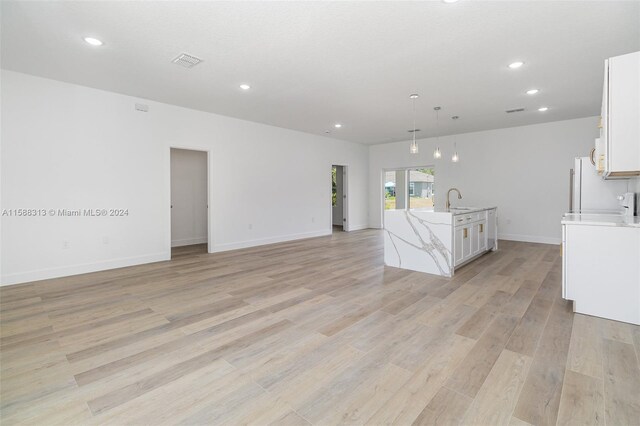 interior space with light wood-type flooring, white cabinets, sink, hanging light fixtures, and a center island with sink