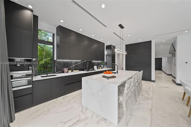 kitchen with a center island with sink, pendant lighting, sink, tasteful backsplash, and light tile floors